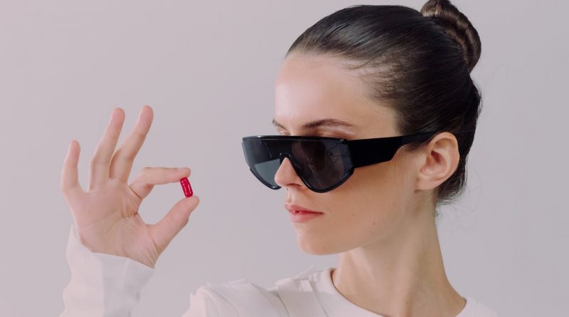 studio shot of woman in sunglasses holding red pill